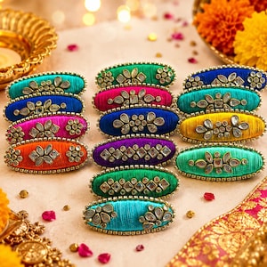 May include: A collection of oval-shaped hair clips wrapped in vibrant silk thread in shades of teal, blue, magenta, orange, green, purple, and yellow, each embellished with clear, faceted stone accents arranged in floral and geometric patterns.
