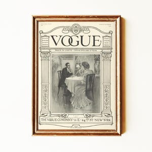 May include: A framed vintage Vogue magazine cover print featuring a black and white illustration of two people seated at a table. The text reads VOGUE, THE VOGUE COMPANY 11 E 24TH ST NEW YORK, and includes volume and price details in a decorative border.
