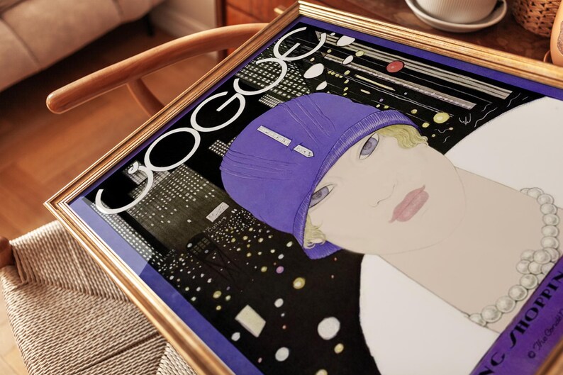 May include: A framed print featuring a stylized illustration of a person wearing a purple cloche hat and a pearl necklace. The background depicts a dark cityscape at night with illuminated windows. The text "VOGUE" is printed in large white letters.
