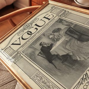 Op de afbeelding: Een ingelijste vintage Vogue tijdschriftomslag uit juli 1893, met een zwart-wit illustratie van twee personen aan een tafel. De print bevat de tekst VOGUE, PRICE 10 CENTS, FOUR DOLLARS A YEAR en 4 JULY 1893, geplaatst in een gouden lijst.