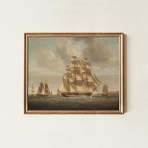 May include: A framed oil painting depicting a large three-masted sailing ship with white sails fully unfurled on a choppy sea. Smaller sailing vessels are visible in the distance under a cloudy sky. The artwork is enclosed in a thin gold frame.