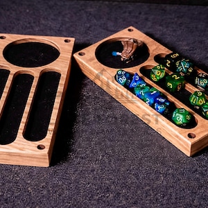 May include: Two wooden dice trays with a dark felt interior. One tray has a circular indentation and three rectangular slots. The other tray holds several multi-sided dice in shades of green and blue, with white numbering.