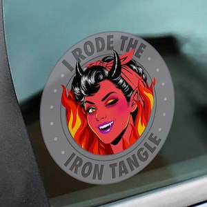 May include: A round, gray sticker with the text "I Rode The Iron Tangle." The sticker features a cartoon illustration of a devil woman with red skin, black horns, and a red headband, surrounded by flames.