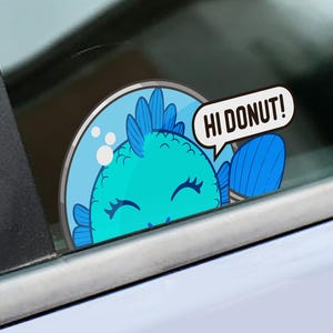 Può includere: Un adesivo circolare in vinile raffigurante un pesce dei cartoni animati blu brillante all'interno di una boccia di vetro. Il pesce ha un'espressione sorridente con gli occhi chiusi e agita una pinna. Un fumetto bianco riporta HI DONUT!