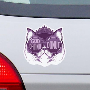 May include: A purple car sticker featuring a cat wearing sunglasses and a crown. The text on the sticker reads "GOD DAMNIT DONUT". The sticker is affixed to the rear of a white car.