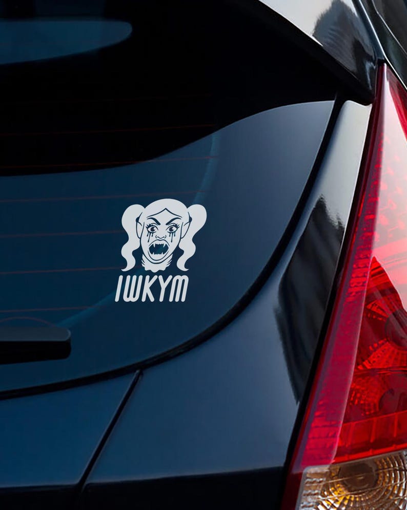 May include: White vinyl car decal featuring a stylized vampire-like character with pigtails, fangs, and tears. The text "IWKYM" is below the graphic. The decal is affixed to the rear window of a dark blue car.