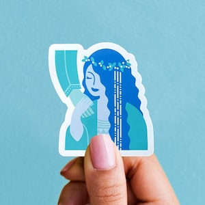 May include: A sticker featuring a stylized illustration of a woman with long blue hair, a floral crown, and a teal dress. The sticker is held by a hand against a light blue background.
