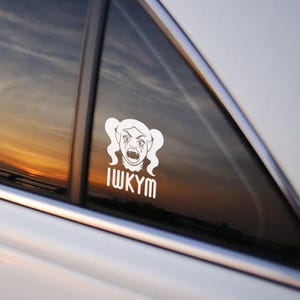 May include: White vinyl decal of a vampire-like character with pigtails, tears, and fangs. The text "IWKYM" is below the character. The decal is affixed to a car window, with a sunset visible in the background.