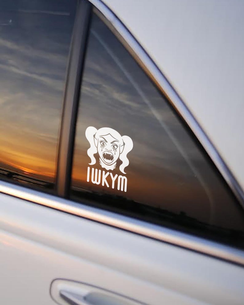 May include: White vinyl decal of a vampire-like character with pigtails, tears, and fangs. The text "IWKYM" is below the character. The decal is affixed to a car window, with a sunset visible in the background.