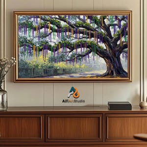 May include: A framed painting depicts a large tree adorned with colorful beads, reminiscent of a festive celebration. The artwork features a road, fence, and buildings in the background, with a gold frame. The painting is displayed above a wooden cabinet.