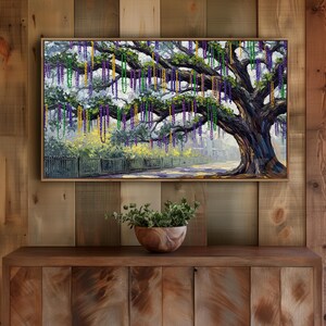 May include: A framed painting depicts a large tree adorned with purple, green, and gold beads, reminiscent of Mardi Gras. The tree's branches are heavy with the colorful strands, set against a backdrop of a fence and a distant street.