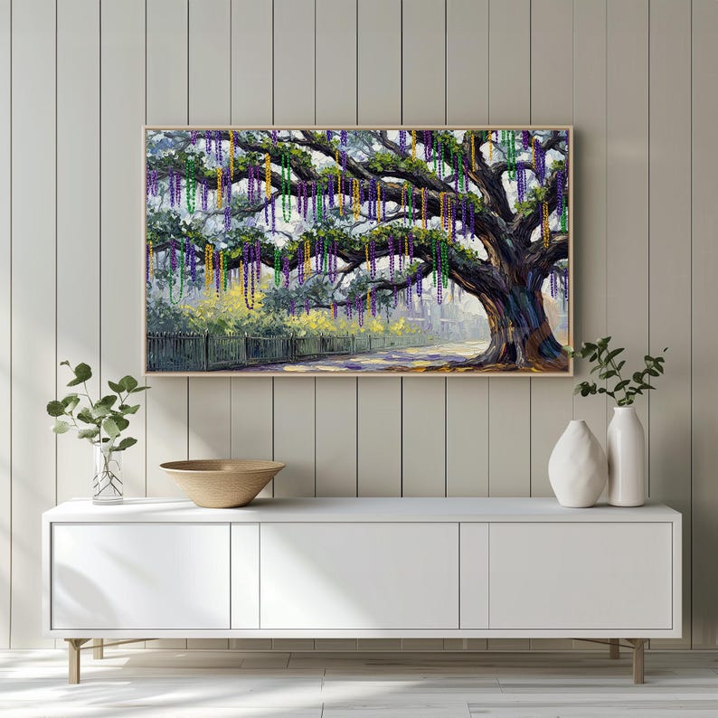 May include: A framed painting depicts a large tree adorned with colorful Mardi Gras beads. The tree's branches are draped with strands of purple, green, and gold beads. The painting has a wooden frame and is displayed on a white cabinet.