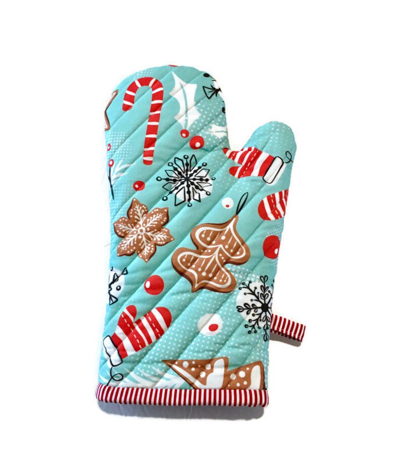 May include: A quilted oven mitt with a light blue background and a repeating Christmas-themed pattern. The pattern includes gingerbread cookies, candy canes, snowflakes, and red accents. The mitt has a red and white striped trim and a small loop.