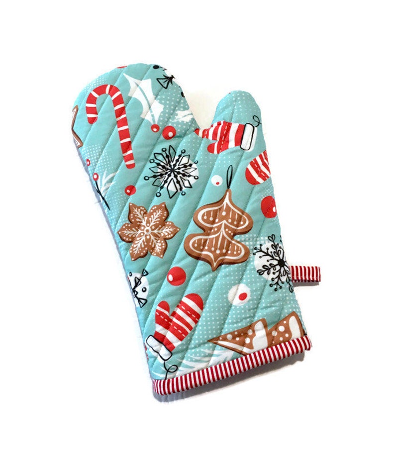 May include: A quilted oven mitt with a light blue background and a repeating Christmas-themed pattern. The pattern includes red and white candy canes, gingerbread cookies, snowflakes, and red berries. The mitt has a red and white striped trim.