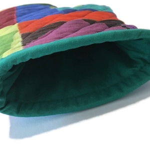 May include: A quilted bucket hat with a patchwork design. The hat features a vibrant mix of colours, including red, blue, green, and purple. The interior and brim are a solid teal green colour.