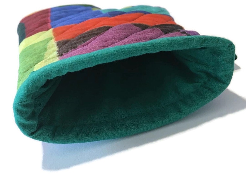 May include: A quilted bucket hat with a patchwork design. The hat features a vibrant mix of colours, including red, blue, green, and purple. The interior and brim are a solid teal green colour.