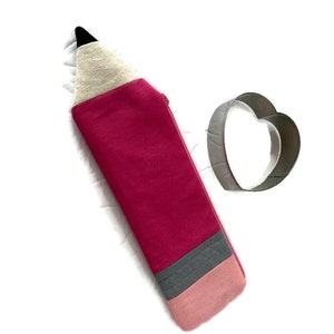 This photo shows a red pencil-shaped pencil pouch with red zipper and heart-shaped cookie cutter.