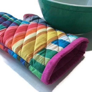 Colorful mod stripes in alternating horizontal and vertical displays are used in this handmade quilted oven mitt lined with magenta solid cotton fabric. A green bowl is a photo prop.