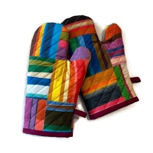 May include: A pair of quilted oven mitts with a patchwork design. The mitts feature a vibrant array of colors including blue, yellow, orange, and purple. The edges are trimmed with a dark pink binding.