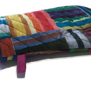 May include: A quilted oven mitt with a patchwork design. The mitt features a variety of colorful fabrics in stripes and squares, including red, orange, yellow, blue, and green. A magenta trim and hanging loop complete the design.