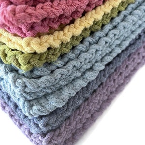 May include: A stack of colorful, braided knit fabric in shades of pink, yellow, green, blue, and purple. The close-up shot highlights the texture and color variations of the material, with each layer neatly stacked on top of the other.