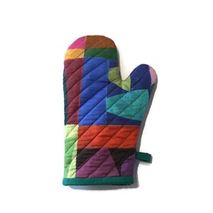 This colorful modern oven mitt makes a bold statement with large patches of saturated colors - blues, oranges, purple, green, pink, yellow. The handmade oven mitt is quilted. The binding and hanging loop are green.