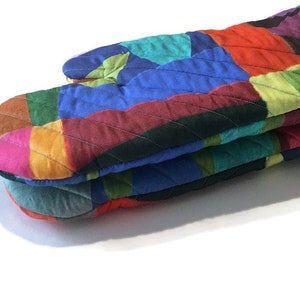 May include: A vibrant, quilted oven glove with a patchwork design. The glove displays a spectrum of colours, including red, blue, green, and pink. Constructed from quilted fabric, it's designed to shield hands from heat in the kitchen.