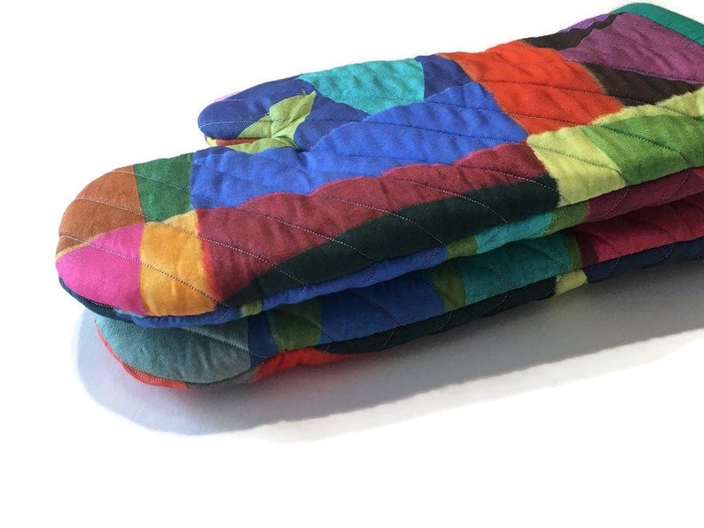 May include: A vibrant, quilted oven glove with a patchwork design. The glove displays a spectrum of colours, including red, blue, green, and pink. Constructed from quilted fabric, it's designed to shield hands from heat in the kitchen.