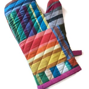 May include: A quilted oven mitt with a patchwork design. The mitt features a variety of colors, including blue, green, red, orange, and yellow, arranged in a striped and checkered pattern. The edges are trimmed with a bright pink binding.