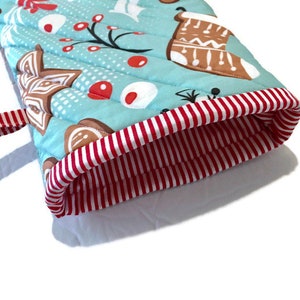May include: A quilted oven mitt with a light blue background and a Christmas-themed pattern. The pattern includes gingerbread cookies, red berries, and white snowflakes. The cuff is red and white striped, and there is a red and white striped loop.