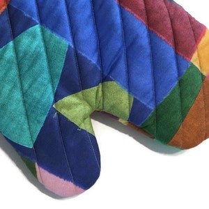 May include: A colourful quilted oven mitt with a patchwork design. The mitt features a variety of colours, including red, blue, green, and pink, arranged in a geometric pattern. The mitt is designed to protect hands from heat.