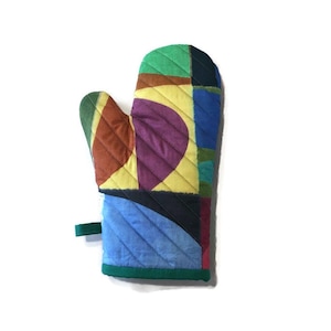 May include: A colourful quilted oven mitt with a patchwork design. The mitt features green, yellow, purple, blue, and brown geometric shapes. It has a green loop for hanging and a green trim around the edge.