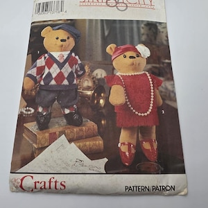 May include: Simplicity 8265 sewing pattern envelope featuring two teddy bears. One bear wears a blue cap, argyle sweater vest, and shorts. The other bear wears a red headband with a white flower, a red dress, and a pearl necklace with red shoes.