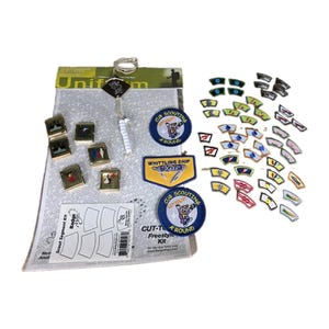 May include: A Cub Scouting badge kit featuring a rectangular instructional sheet, two circular embroidered patches, one rectangular Whittling Chip patch, six square metal pins, and numerous small curved segment patches in various colors.