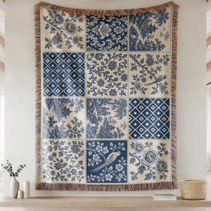Pode incluir: Uma manta tecida retangular com um design de patchwork em azul e creme. O padrão inclui vários motivos como vinhas florais, diamantes geométricos, pássaros e cenas de paisagens com pagodes, finalizada com uma borda de franjas.