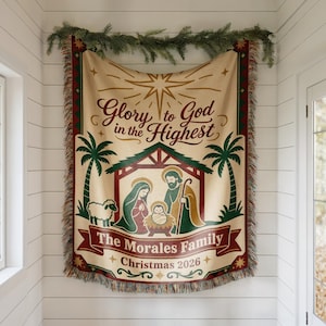 Könnte beinhalten: Eine gewebte Wohndecke mit einer Krippenszene, die Maria, Josef und das Jesuskind unter einem Stern zeigt. Der Text lautet Glory to God in the Highest, The Morales Family und Christmas 2026. Das Design enthält Palmen und Fransen.
