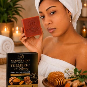 Peut inclure: Un savon rectangulaire de couleur orange avec le logo Nanoustore gravé sur le devant. À côté, une boîte noire étiquetée Turmeric & Honey Brightening Soap, 100g, illustrée avec de la racine de curcuma et un rayon de miel, et un bol en bois.