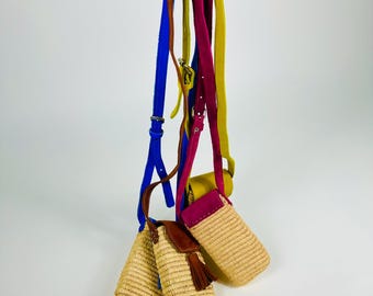 May include: Three woven straw phone bags with colorful straps in blue, brown, pink, and yellow. Each bag has a different colored strap and a leather flap. One bag has a brown tassel.