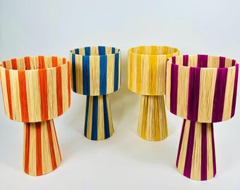 May include: Four decorative planters with a striped design. Each planter features a cylindrical top and a flared base. The planters are in various colors: orange and beige, blue and beige, yellow and beige, and purple and beige.