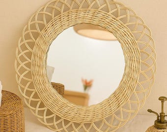 May include: A round, woven rattan mirror with a decorative, scalloped edge. The mirror is surrounded by a light beige frame. A woven tissue box and a small, decorative water sprayer are also visible.