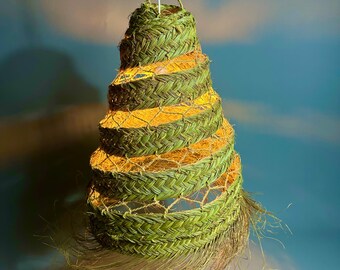 May include: A hanging, woven lamp with a spiral design. The lamp is made of green and tan woven material, with a chain for hanging. The lamp's interior glows with a warm, yellow light, creating a decorative and natural aesthetic.