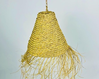 May include: A woven, conical pendant light fixture. The light is made of natural-colored woven material, with a flared shape and a fringe of loose strands at the bottom. It hangs from a gold-colored chain.