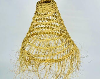 May include: A woven pendant light fixture with a conical shape, crafted from natural-colored straw. The light fixture is suspended from a gold-colored chain. The bottom edge features loose, dangling strands, adding a textured, organic aesthetic.