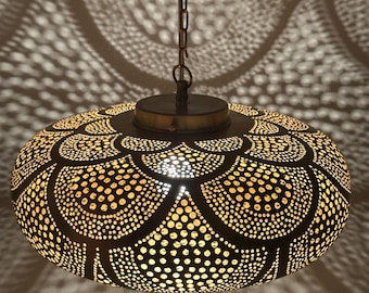 May include: A decorative, hanging pendant light with a dark metal finish. The light has an intricate, perforated design that casts a patterned shadow on the surrounding surface. The light is suspended by a chain.