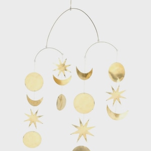 Può includere: Un mobile a tema celeste con stelle, lune e forme circolari color oro sospese a un telaio metallico curvo. Questo elemento decorativo da appendere è progettato per aggiungere un tocco di fantasia a qualsiasi stanza.