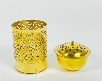 May include: Two gold-colored decorative items. One is a cylindrical container with intricate cut-out patterns. The other is a small, round bowl with a lid, also featuring cut-out designs. Both items have a shiny, metallic finish.