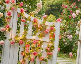 May include: A white wooden garden gate adorned with pink rose garlands and small lights. The roses are in full bloom, and the green leaves provide a natural contrast. The background features a lush garden with more roses.