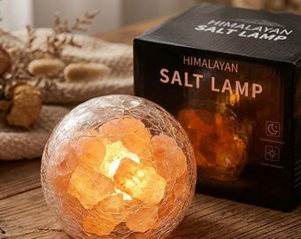 May include: A spherical Himalayan salt lamp with a cracked glass exterior containing glowing orange salt chunks, positioned next to a black product box labeled HIMALAYAN SALT LAMP with icons for night and day settings.