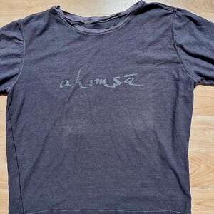 May include: A dark gray long-sleeved t-shirt with the word "ahimsa" printed in a light gray color on the front.