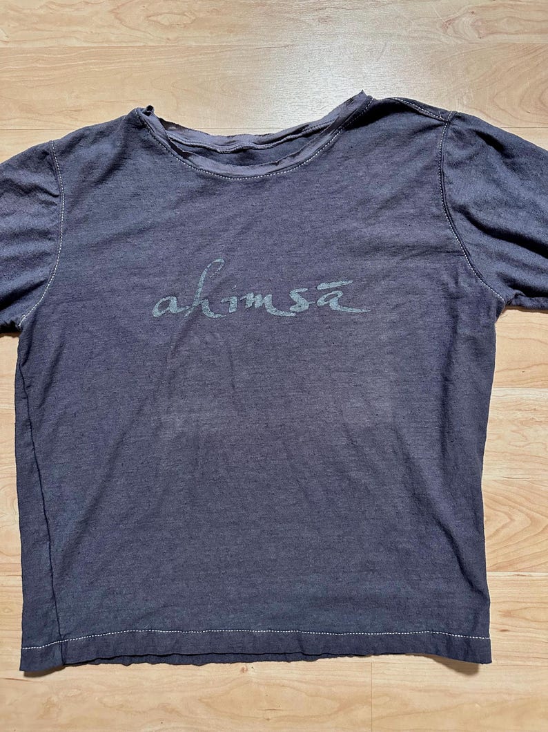 May include: A dark gray long-sleeved t-shirt with the word "ahimsa" printed in a light gray color on the front.